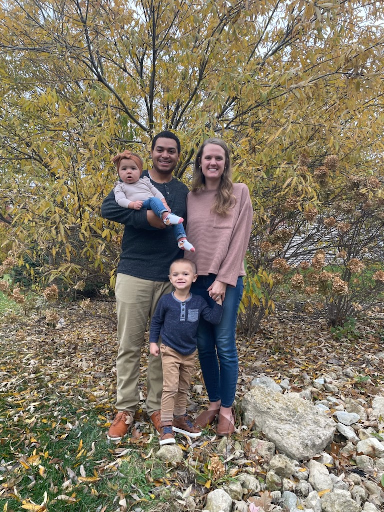 A couple with two children standing outside by a tree in fall